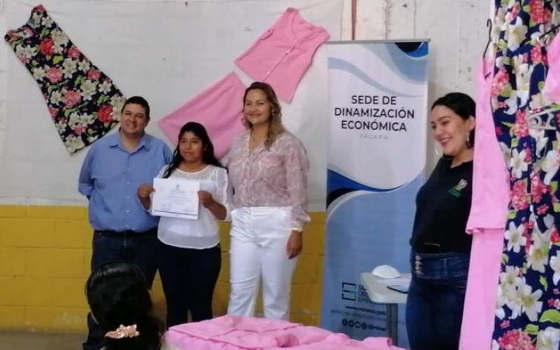 4 personas posan sobre fondo con imagen del Ministerio de Economía recibiendo diplomas 