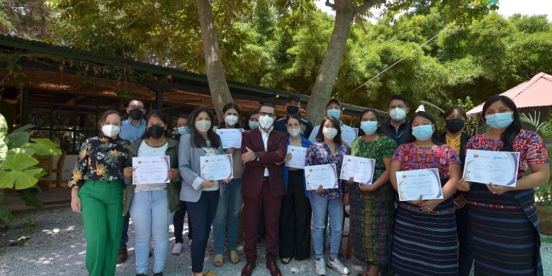 Grupo de Personas entre hombre y mujeres, tienen como fondo un árbol, reciben reconocimientos por capacitación
